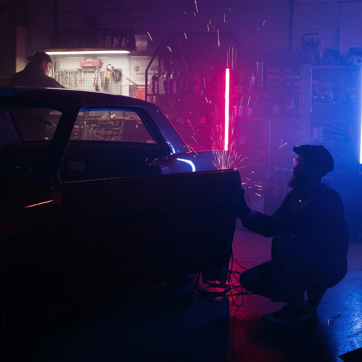 A mechanic working on a classic car with sparks flying in a garage, illustrating automotive writing.