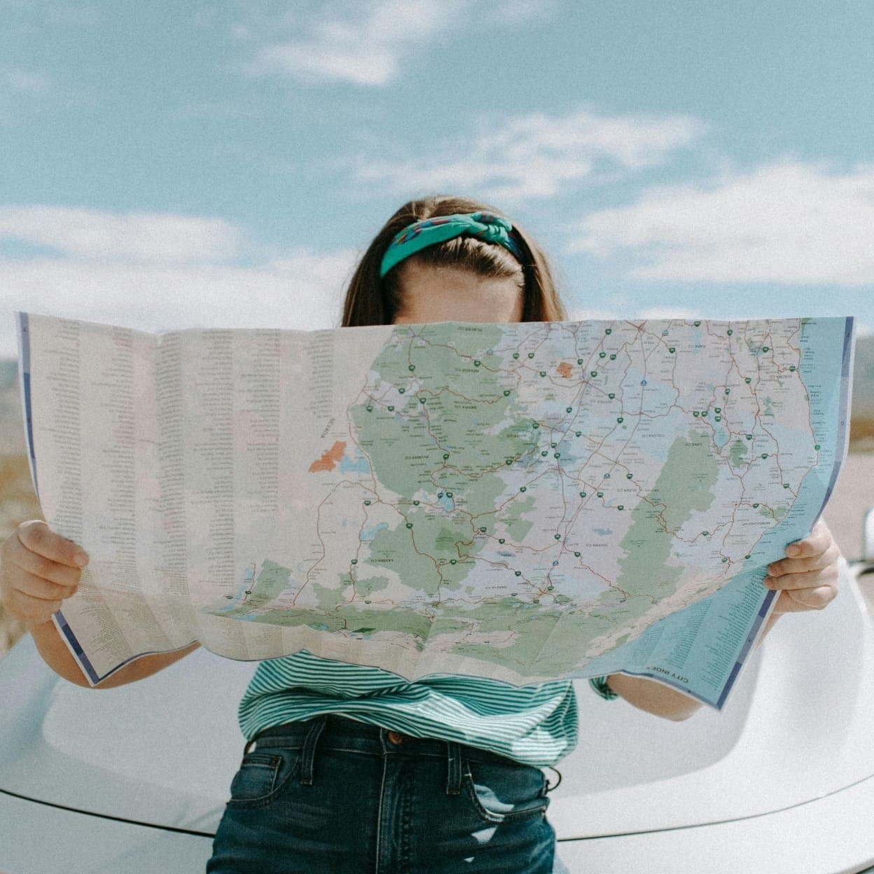 A person holding an unfolded road map beside a car on a road trip, illustrating travel writing.