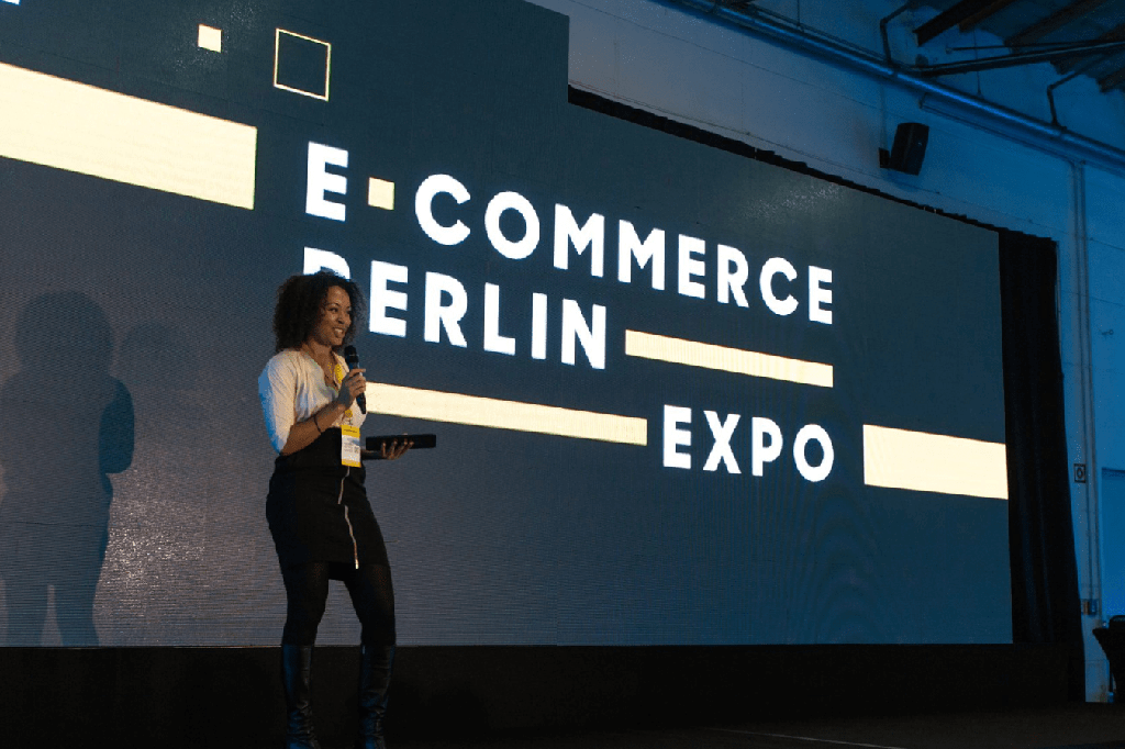 A speaker presenting on stage in front of an "E-Commerce Berlin Expo" 2022 screen.