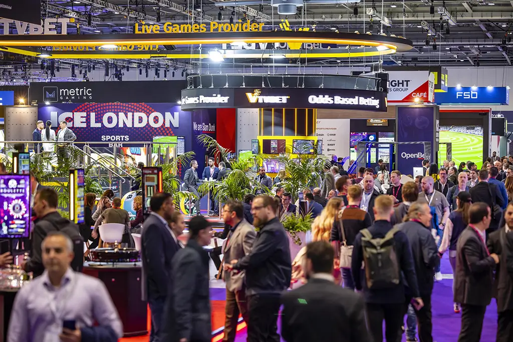 Crowds of attendees networking among lit gaming booths on the show floor at ICE London 2022.