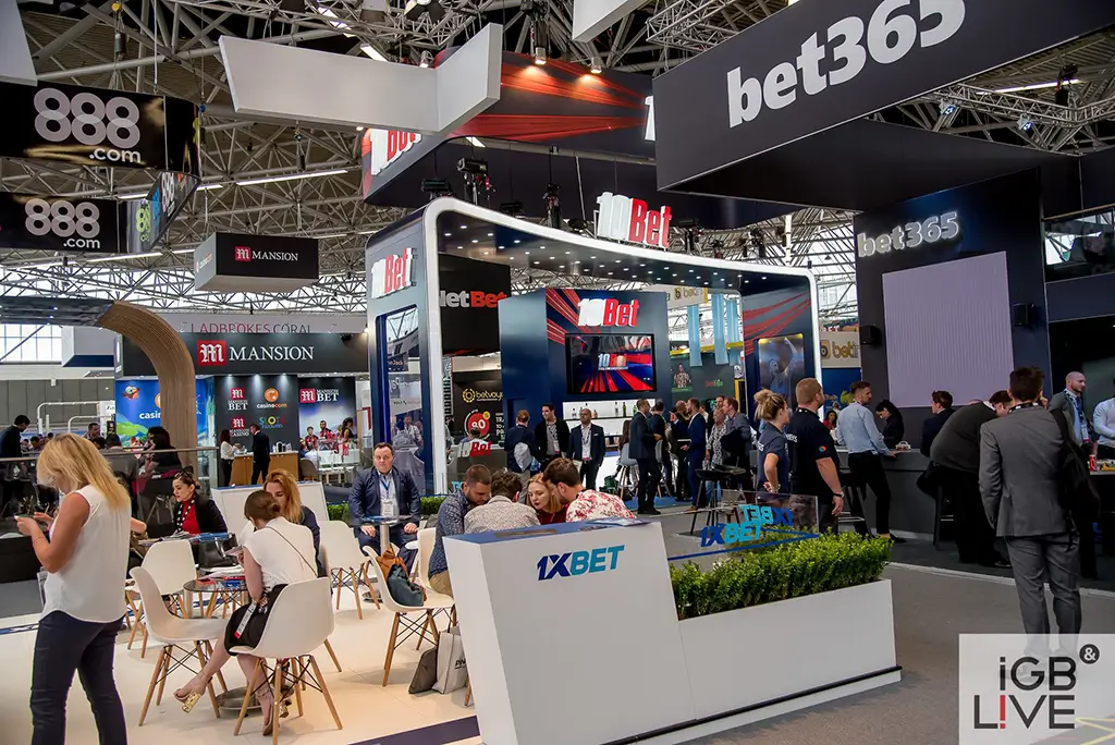 A busy iGB Live 2018 exhibition floor with branded iGaming booths and attendees networking at stands.