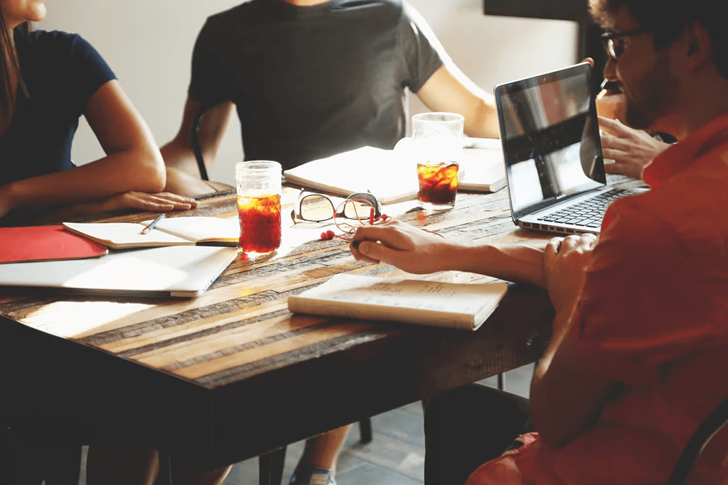 A team collaborating around a laptop and notebooks at a sunlit wooden table while planning SEO content.