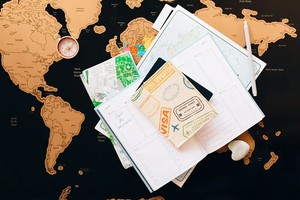 Flat lay of a travel journal, city maps and compass on a scratch map, representing travel website SEO planning.